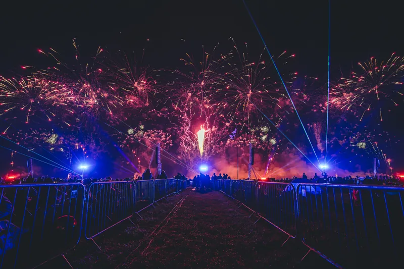An audience watching pink and gold fireworks with blue lighting and lasers