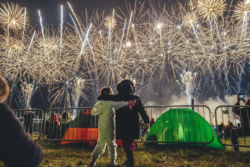 Two children embracing as a huge golden fireworks display fills the sky